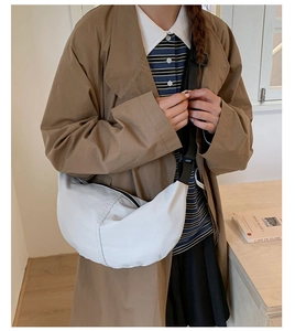Detail view of a white crescent crossbody bag with black fabric strap worn on trench coat