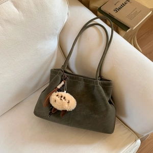 Olive green matte shoulder bag with soft plush pendant on a minimal fabric sofa