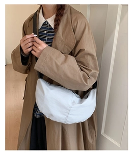Detail view of white crescent bag with black adjustable strap worn with a trench coat