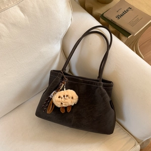 Detail of dark brown suede tote bag with plush sheep charm on a cream fabric sofa