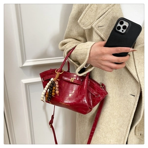 Dettaglio borsa a secchiello rossa coccodrillo con chiusura dorata e ciondolo su tweed