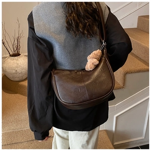 Detail of dark brown faux leather saddle bag featuring a cute plush bear pendant accessory