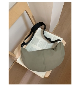 Olive green crescent crossbody bag on a wooden chair with an open book in detail