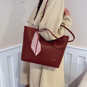 Détail d'un sac cabas bordeaux avec un élégant foulard en soie noué sur la poignée