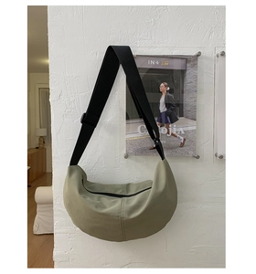 Detail of sage green crescent crossbody bag hanging on a minimalist white textured wall