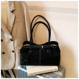 Détail d'un sac cabas noir avec surpiqûres blanches sur une valise argentée
