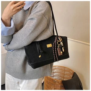 Detail of black faux leather tote bag featuring golden buckle and striped ribbon charm