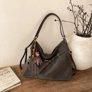 Detail der grauen Retro-Tasche mit Fransenquaste und Bärenanhänger auf einem Holztisch