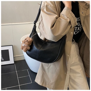 Detail of black pebbled leather crescent tote bag with a cute brown bear charm