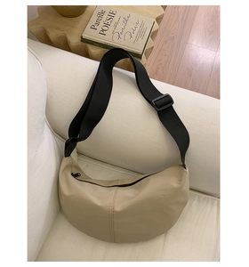 Detail of beige crescent crossbody bag on sofa showing nylon texture and wide black strap