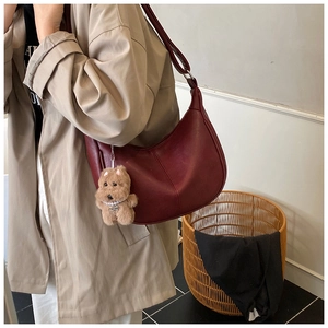 Detail view of burgundy crescent bag with soft PU leather and plush dog accessory