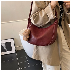Detail of burgundy hobo bag with leather texture and a cute brown plush bear charm