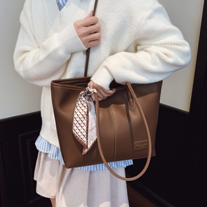 Détail d'un grand sac cabas marron en cuir avec un foulard décoratif et logo de mode