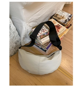 Detailed close-up of cream crescent crossbody bag with black adjustable strap on floor