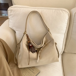 Detail einer cremeweißen Hobo-Tasche mit Seitenschnalle und Bärenanhänger auf Sofa