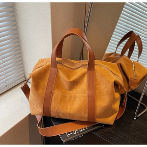 Detail of tan suede tote bag with leather straps and metal hardware on wooden desk