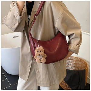 Deep red crescent crossbody bag with lychee texture and plush puppy charm detail