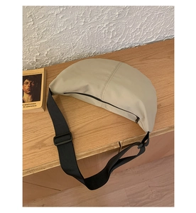 Detail of a beige matte leather crossbody bag showing a wide adjustable nylon strap on wood