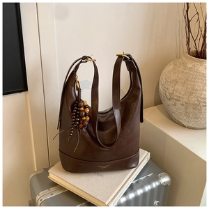 Detail der braunen Retro-Ledertasche mit goldenem Logo und Holzperlen-Quastenanhänger