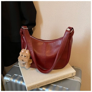 Close-up of a dark red crescent shoulder bag with a cute plush bear charm on books