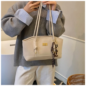 Detail view of cream-white leather tote bag featuring gold buckle and silk scarf charm