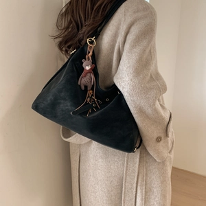 Detailansicht der schwarzen Umhängetasche aus weichem Leder mit Bärenanhänger am Model