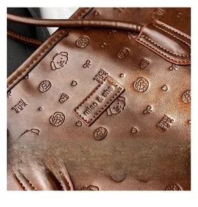 Close-up of brown embossed leather tote with dog and heart patterns and brand logo