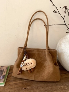 Vintage brown suede shoulder bag for women with cute plush charm on rustic wooden table