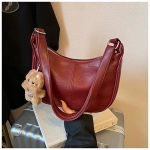 Detail of burgundy leather crescent tote bag with silver zipper and plush dog charm