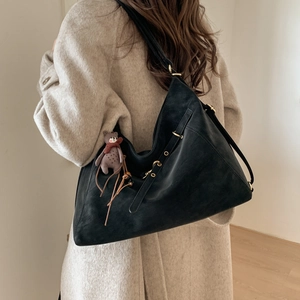 Detailansicht der schwarzen Hobo-Tasche mit Bärenanhänger und Quaste am beigen Mantel