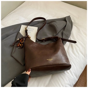 Detail der dunkelbraunen Leder-Eimertasche mit Holzperlen-Quaste und goldenem Logo