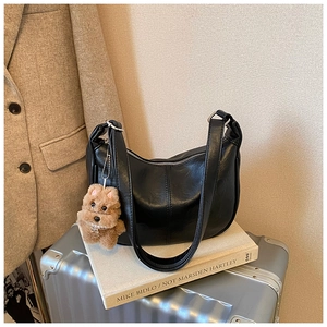 Detail of black faux leather hobo tote bag featuring a cute brown plush puppy bag charm