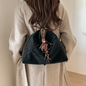 Detail eines großen schwarzen matten Rucksacks mit Bärenanhänger auf einem Wollmantel