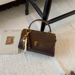 Détail d'un sac à main en cuir marron avec rabat en daim et pompon de perles en bois