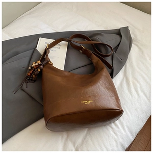 Detail der dunkelbraunen Leder-Eimertasche mit Goldschrift und Vintage-Perlenanhänger