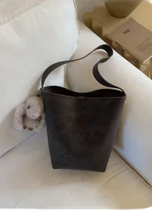 Detail view of a dark brown tote bag with a soft plush rabbit charm on a sofa