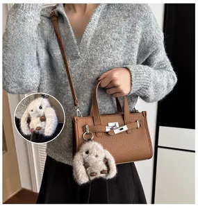 Brown lychee leather handbag featuring a metal turn-lock and grey plush rabbit pendant