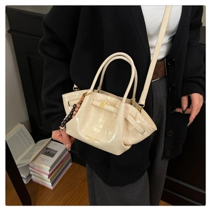 Dettaglio della borsa a secchiello beige coccodrillo con finiture dorate e ciondolo