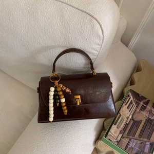 Détail d'un sac à main en cuir marron vintage avec boucle dorée et breloque perlée