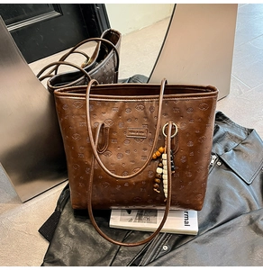 Close-up of embossed patterns and brand tag on dark brown leather tote bag with beads