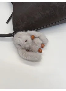 Close-up of a grey plush rabbit charm with leather accents on a brown textured leather bag