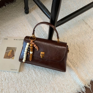 Détail d'un sac à main vintage marron foncé avec texture huilée et breloque en bois