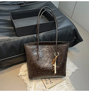 Detail view of deep brown tote bag featuring embossed poodle patterns and beaded charms