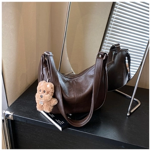 Detail of dark brown faux leather tote bag with plush bear charm and wide strap