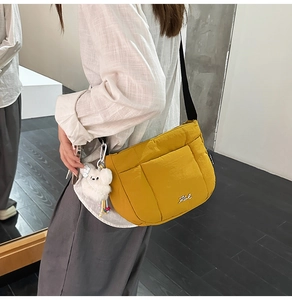 Détail d'un sac seau jaune matelassé avec bandoulière noire et breloque ours en peluche