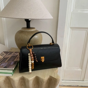 Détail du sac à main en cuir noir avec boucle dorée et perles en bois décoratives
