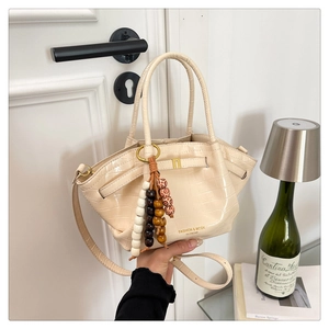 Dettaglio borsa beige a motivo coccodrillo con fibbia a H dorata e ciondolo con perline