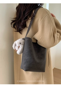Detail of dark grey bucket bag with plush bunny charm and textured leather finish
