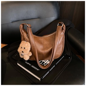 Detail view of a vintage brown leather crescent tote bag with a plush puppy keychain