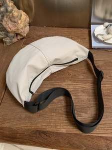 Minimalist beige nylon crescent crossbody bag with black adjustable strap on wooden table